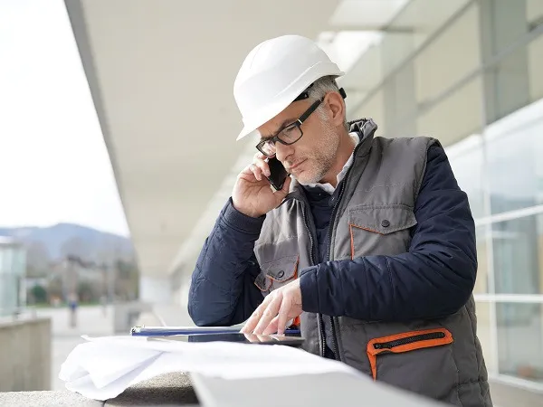 Ingenieur telefoniert mit Planunterlagen im Freien